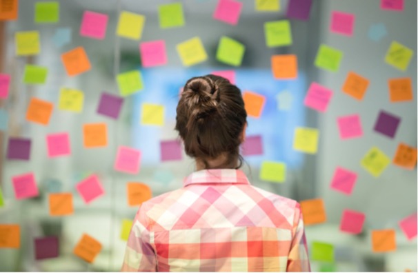 Eine Frau steht vor einer Glaswand an welcher viele Sticky Notes kleben