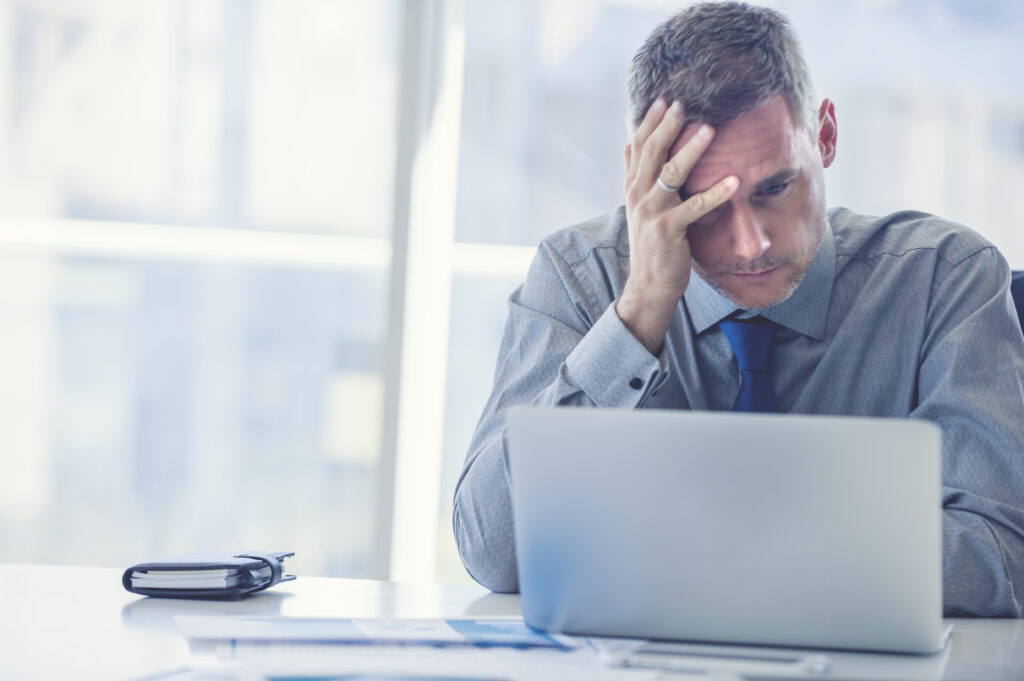 Stressed mature businessman with laptop. He could also have a headache. He is sitting in the boardroom. There are documents on the table.